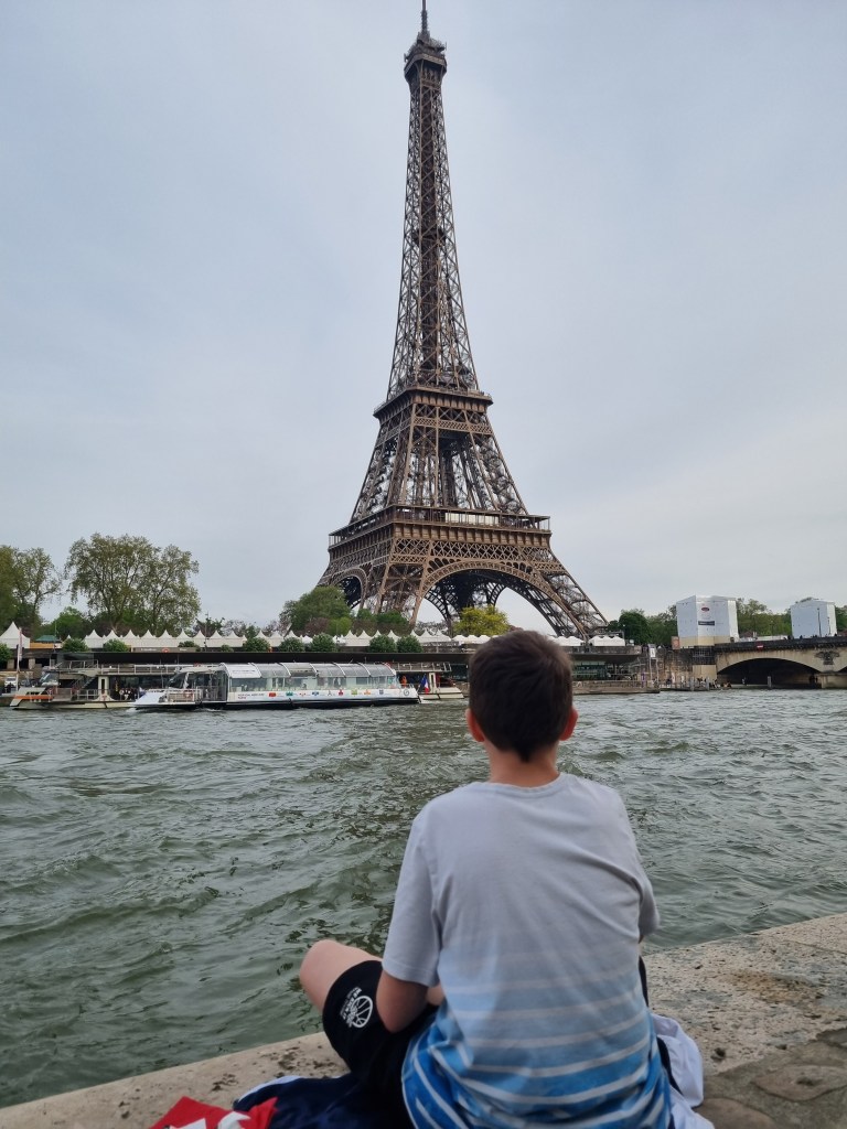 Ein Junge sitzt am Ufer der Seine und blickt auf den Eiffelturm in Paris.
